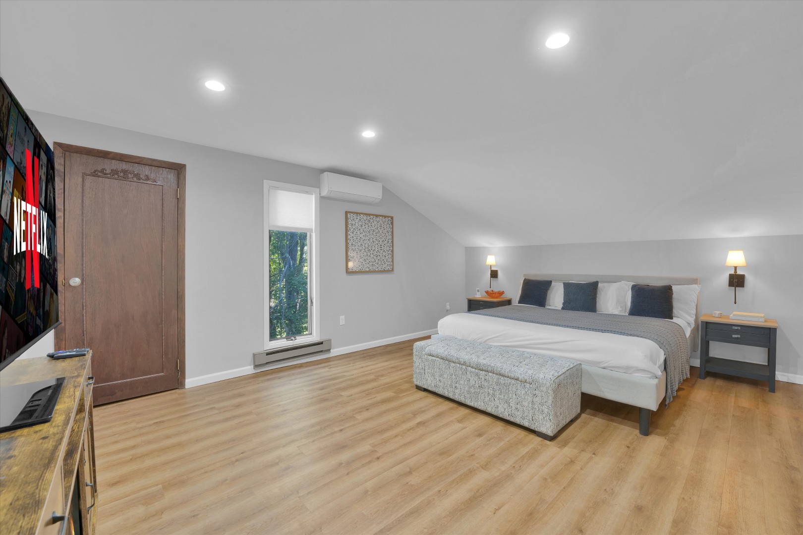 Spacious bedroom suite featuring warm wood flooring, crisp linens, and serene natural views.