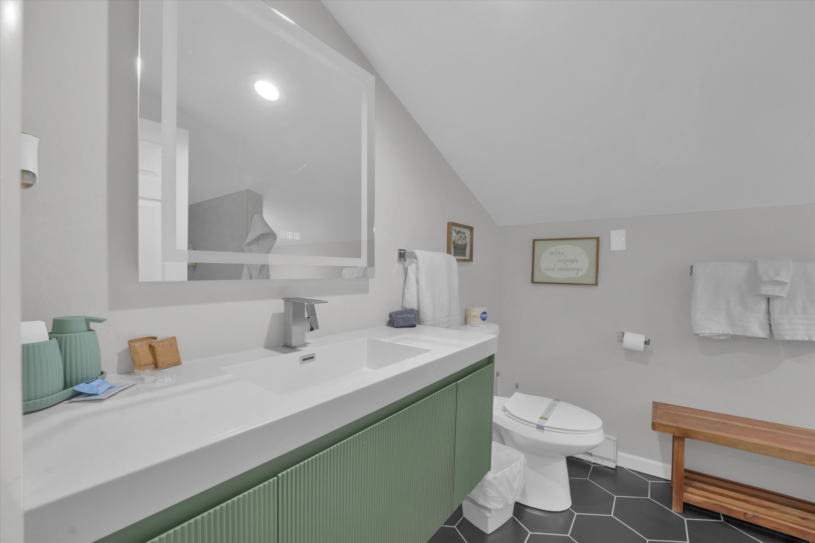 Clean, modern full bathroom featuring a stylish sage green vanity and brightly lit vanity mirror.