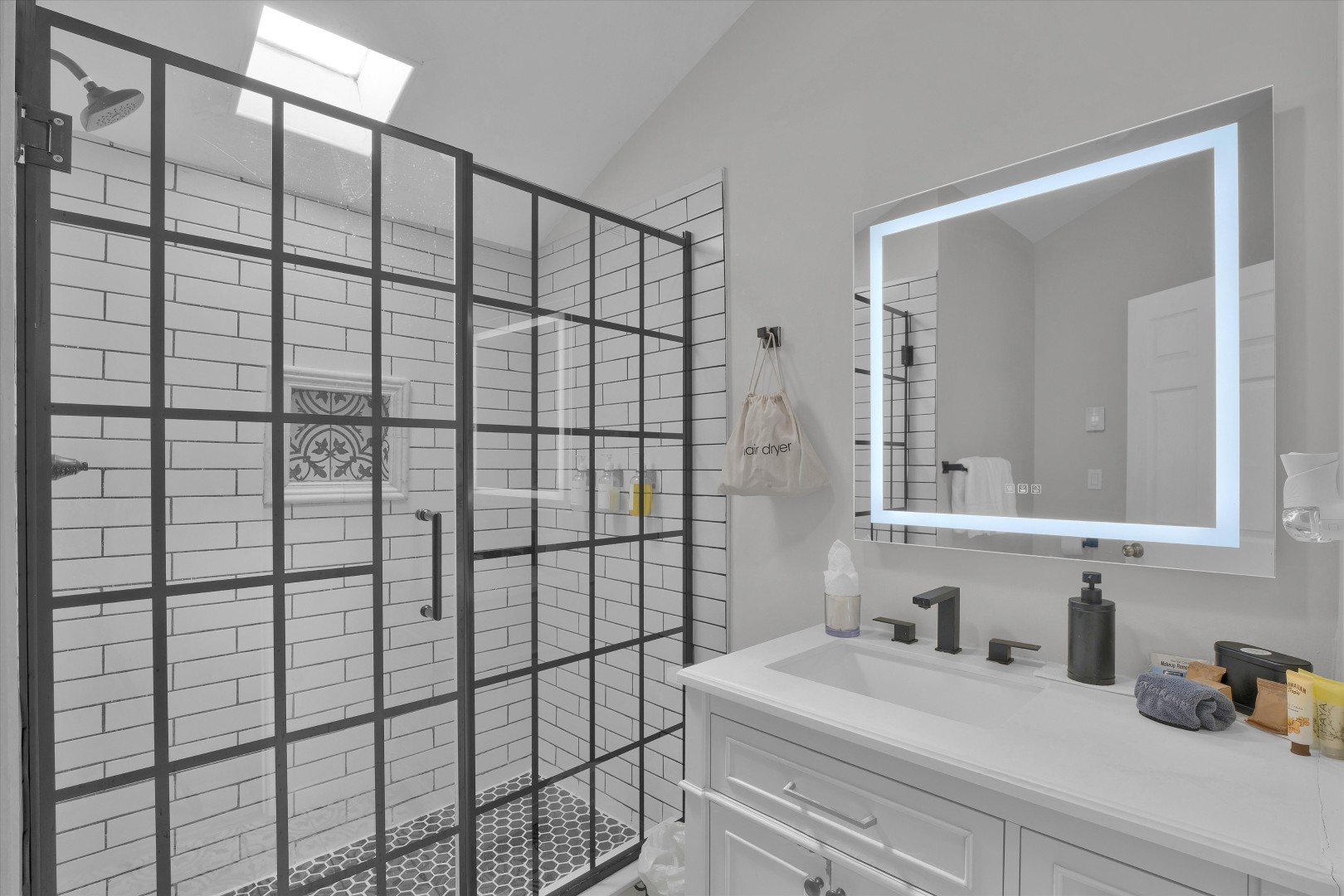Sleek bathroom complete with a black grid glass walk-in shower and backlit LED mirror.