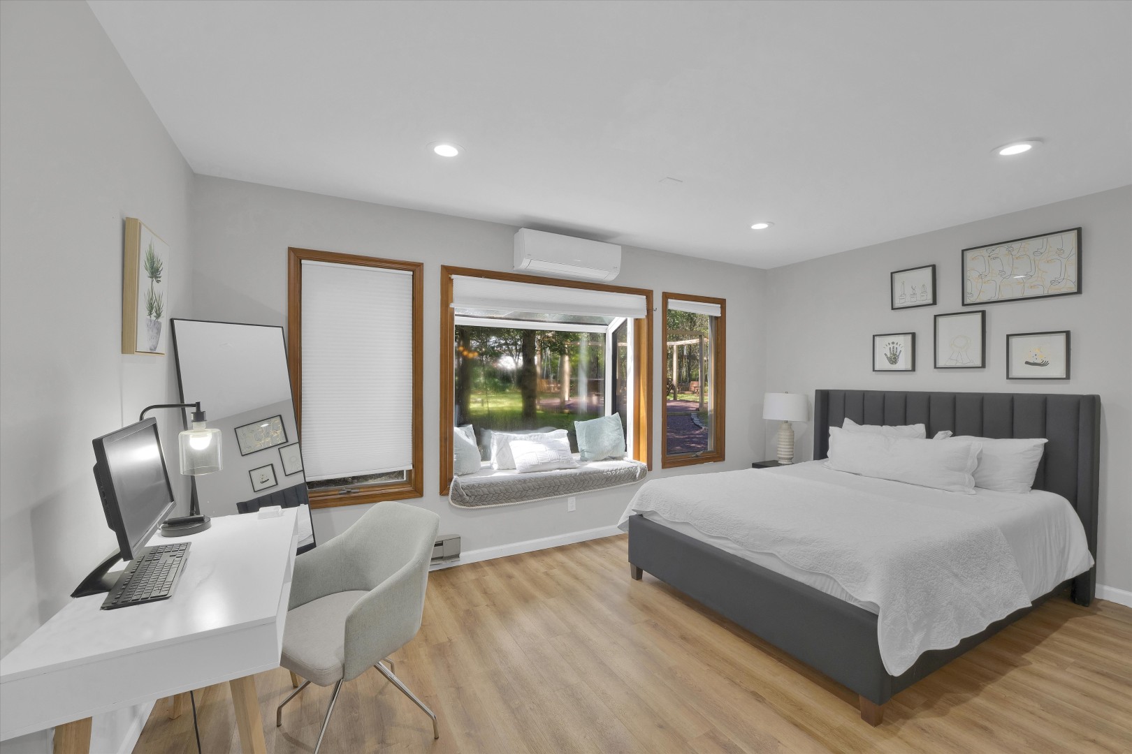 Streamlined bedroom offering a comfortable queen-size bed, warm oak-trimmed windows, and a dedicated workspace.