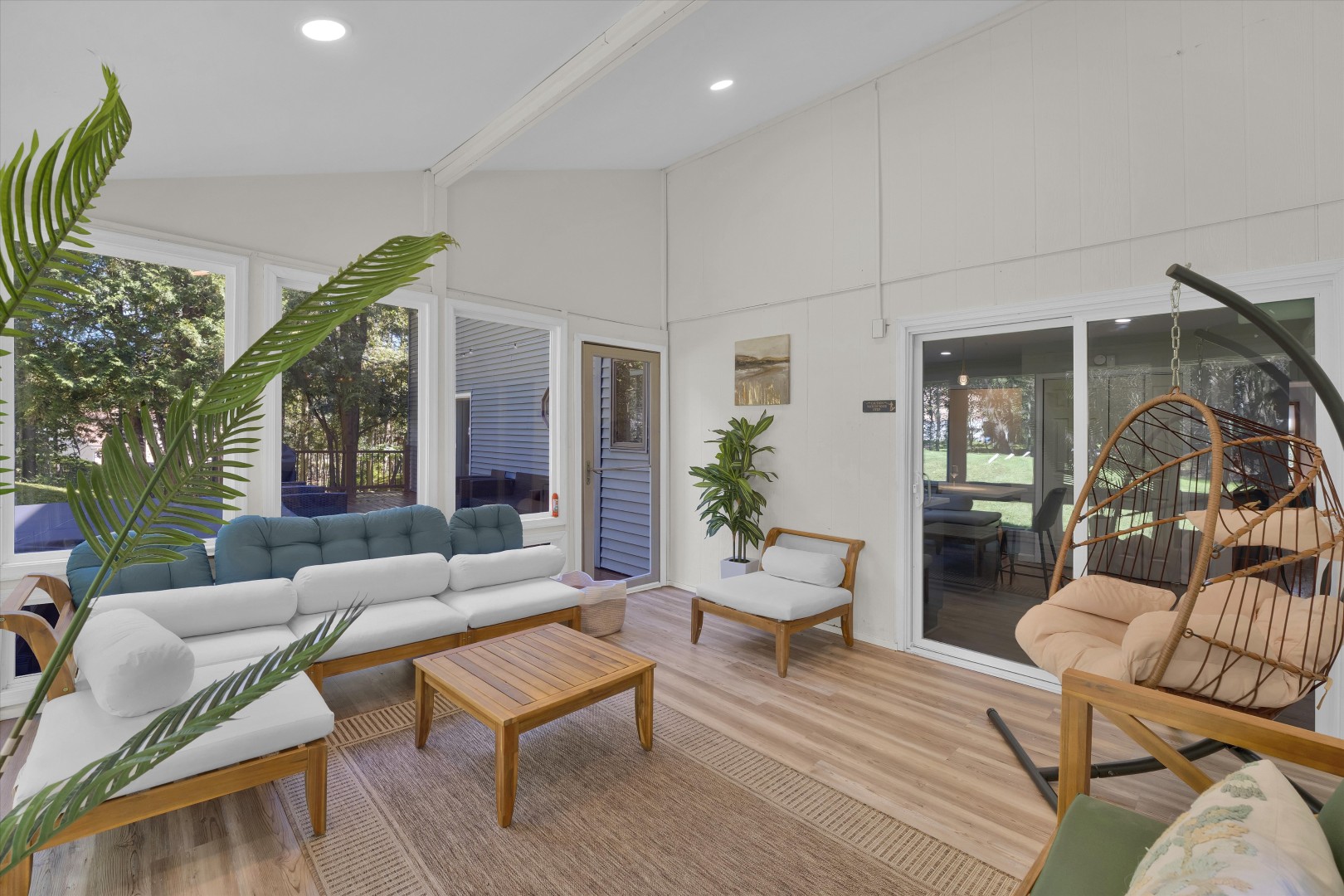 Bask in natural light throughout this airy sunroom retreat, featuring rattan lounge chairs, a hanging egg chair, and garden views.