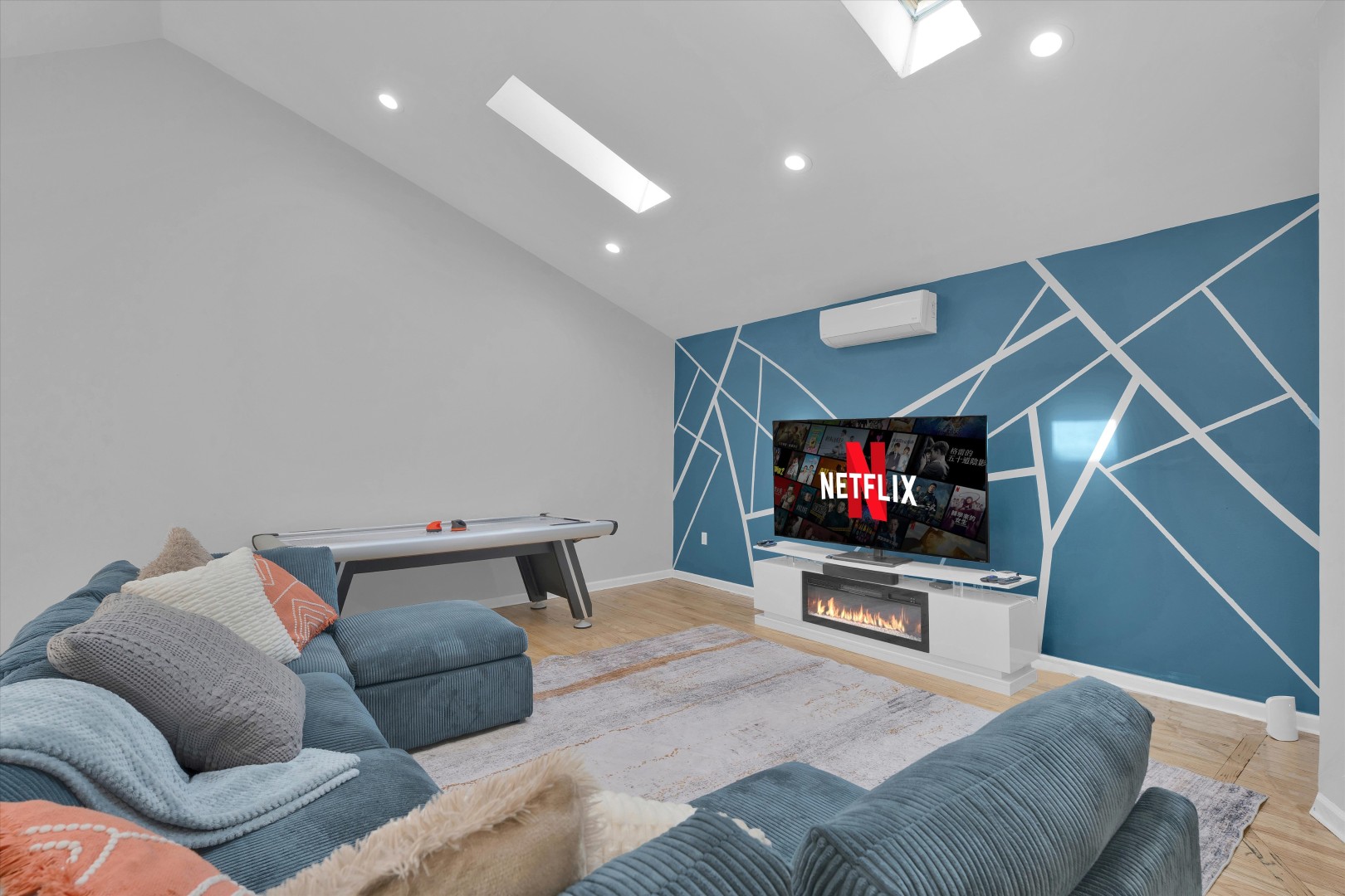 Kick back on the plush sectional in this lounge, featuring a blue geometric wall, air hockey table, and electric fireplace