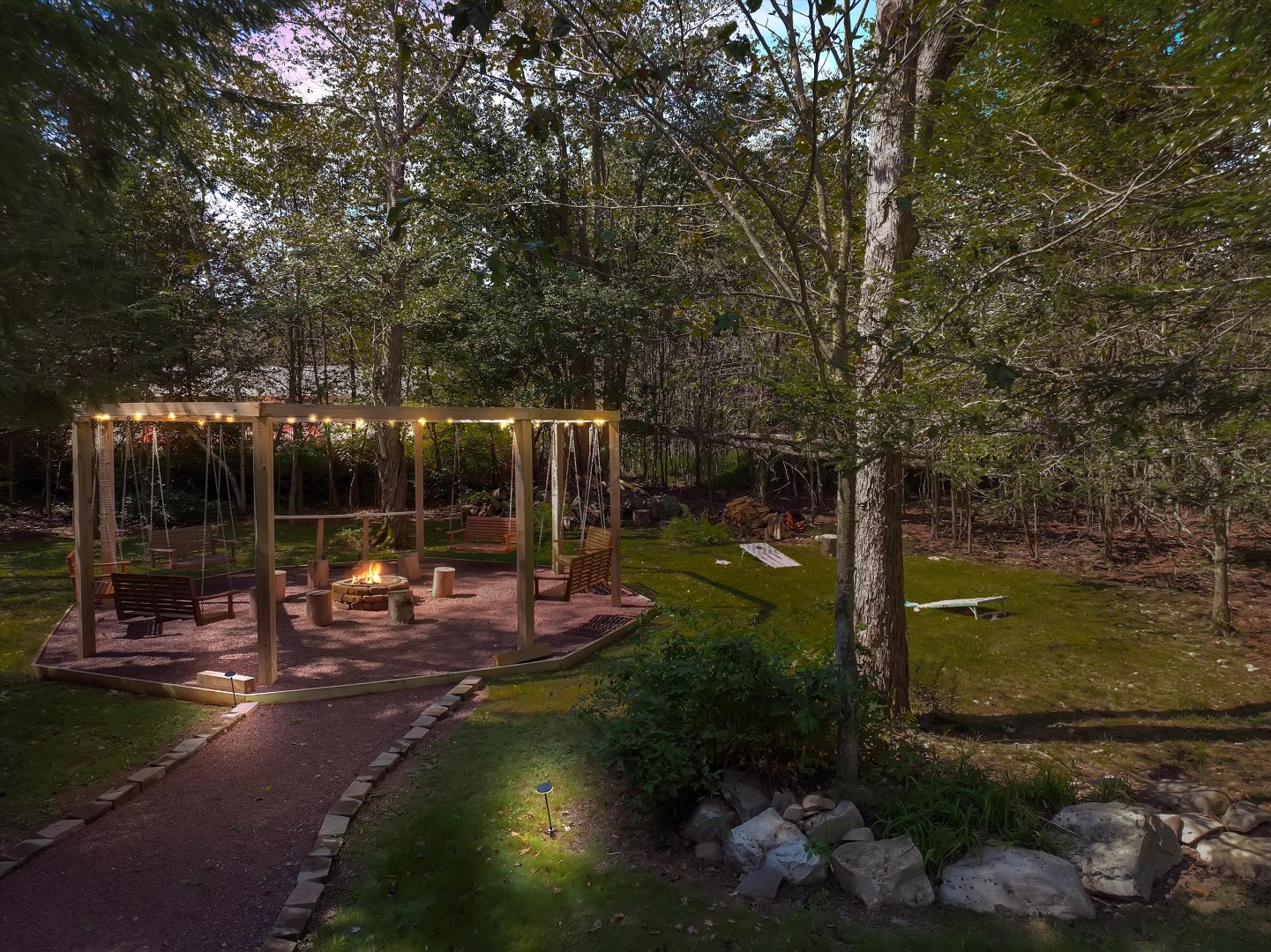 Outdoor fun featuring a custom fire pit with wooden swings and a backyard cornhole game set in a peaceful forest clearing.